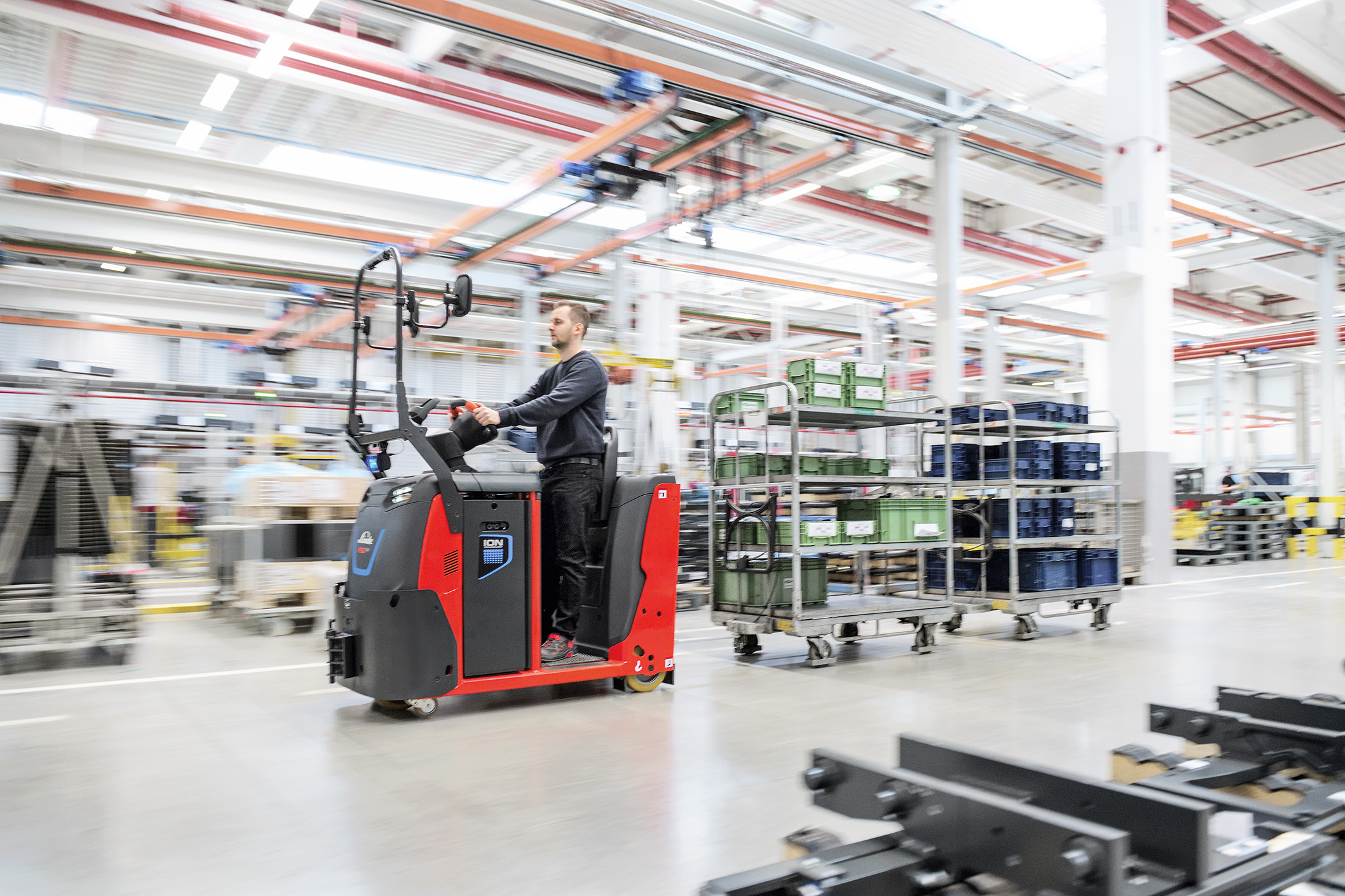 Medewerker Linde rijdt in nieuwe elektrische Linde trekker in magazijn met vracht - Efficiënt intern transport.